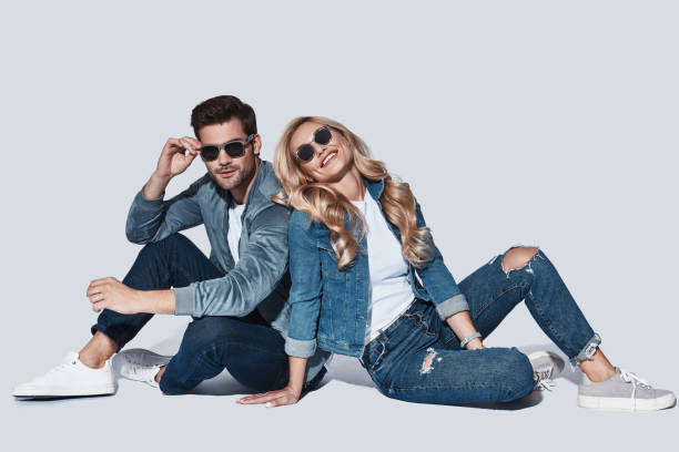 Beautiful young couple in denim wear bonding and smiling while sitting against grey background